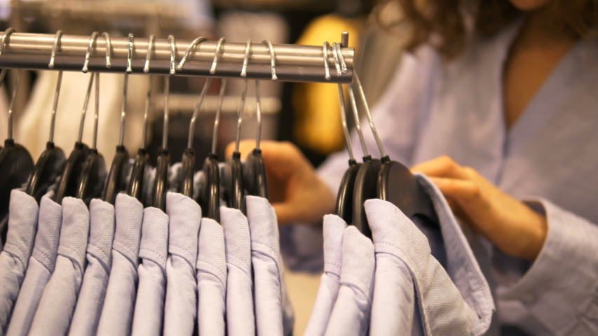 A woman in a clothing store carefully chooses a shirt of the right size, close-up hangers with clothes | Shutterstock HD Video #1040215568