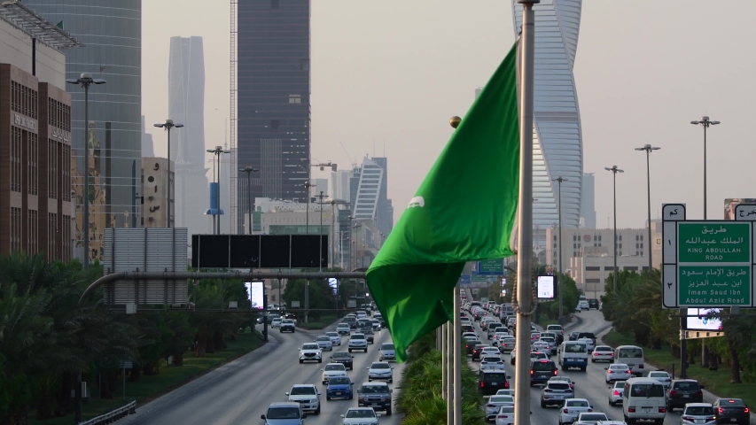 Riyadh, Saudi Arabia – September 25th 2019: Saudi Arabia flag waving and Riyadh's main street on background. 
