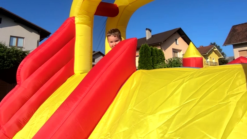 Slow motion small young Caucasian handsome boy playing on inflatable bouncy castle slide