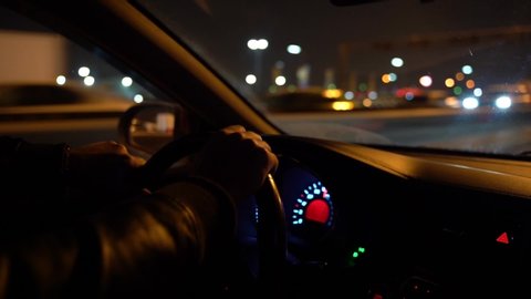 4K Man Driving Car hrough streets of night city. Close-up of a man`s hands lie on the steering wheel of a car. Glare in the window of the car.