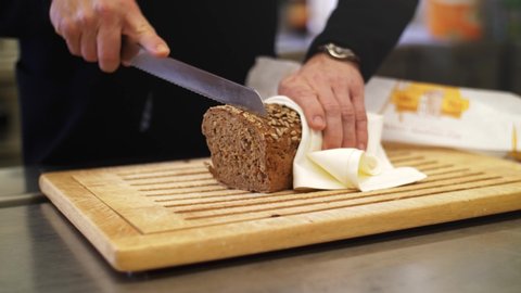 4K Slow motion close up of a a fresh whole-grain bread being sliced with a knife. Grains falling of the loaf, filmed with a wide aperture