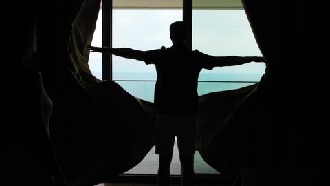couple in hotel room by the sea, man opens curtains, hugging at the window