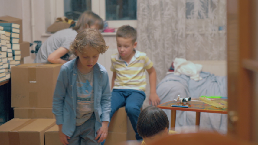 Medium shot of a group of kids playing among boxes in their new home while eating candy