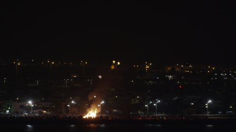 People gathering by the big bonfire on waterfront at night during San Juan Festival in Lanzarote, Canary Islands