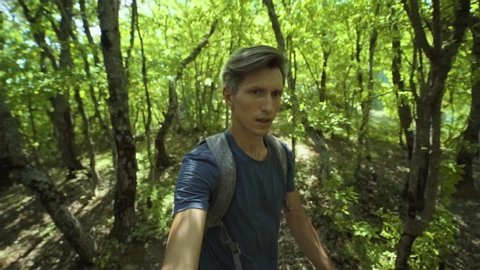 closeup wide angle selfie portrait of young adult man fast walking in forest at summer day. guy runs through a dense forest filming himself on a camera