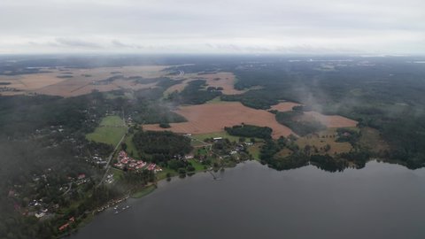Swedish mansion or manor and homes by a lake. landscape view drone passing through clouds showing farmland, fields and forest. Sweden in summertime