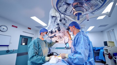 Operation through new microscope in hospital. Two surgeons perform surgery in the neurosurgical department using modern equipment.