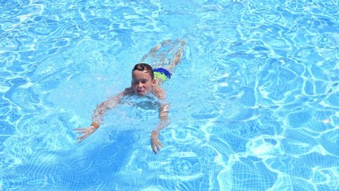 Happy boy swimming outdoors. Cute boy in blue clear water of the swimming pool. Child having joyful time in outdoor water park in summer.