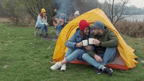 ouple camps in nature with campfire and drinks beverage from vintage white cups