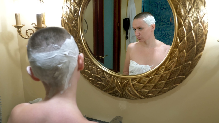 Beautiful bald woman looks in a luxurious bathroom mirror and does her hair, shaves her hair with a dangerous razor | Shutterstock HD Video #1040287007