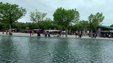 AMSTERDAM - CIRCA JUNE, 2019: Footage of people walking and hanging out around pool at museum quarter (museumplein) in Amsterdam. Camera pans right.