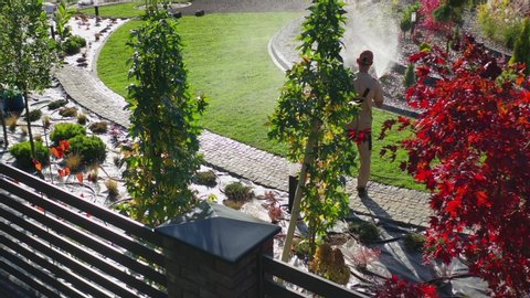 Caucasian Professional Gardener Watering Newly Developed Residential Garden Using a Hose. Sunny Fall Day.