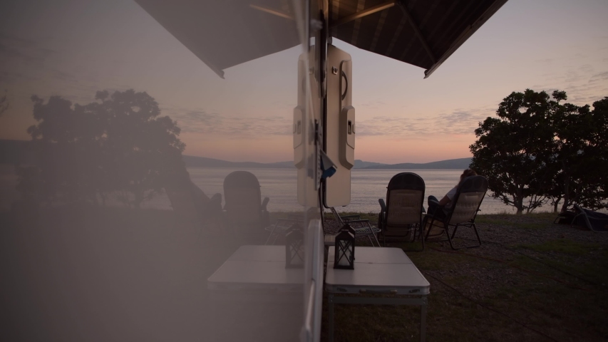 Caucasian Woman Relaxing in Front of Her Motorhome RV Camper Van During Scenic Seafront Sunset. Rving Theme