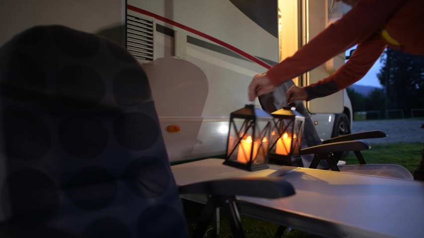 Motorhome Road Trip. Men Placing Camping Lanterns on the Table in Front of His Camper Van. RV Park Theme.