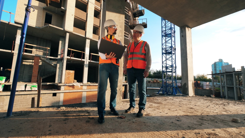 People walk on a construction site with a laptop. Construction workers at modern construction site. Royalty-Free Stock Footage #1040291969