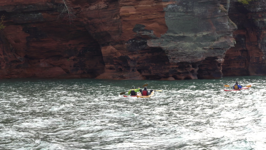 A group of happy, smiling kayakers explore the Apostle Islands sea caves on a fall day on Lake Superior in Wisconson