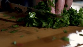 A Close up slow motion footage of cutting parsley on a wooden cutting board 