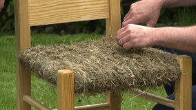 Handheld, medium close up shot of chair seat made of hay, a person trims the hay with a pair of scissors.