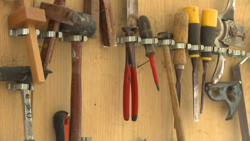 Steady, medium close up shot of tools hanging on a wooden wall.