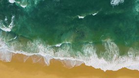 Aerial top view of waves break on tropical yellow sand beach. Sea waves seamless loop on the beautiful sand beach. Ocean surf