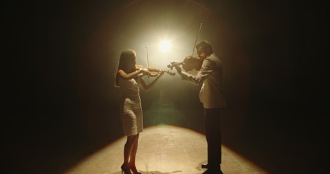 Duet of two professional violin players having a solo together, performing on stage during concert, spotted by light on black background 4k footage