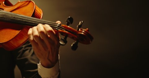 Experienced Violinist performing amazing solo on stage, spotted by light on black background close up 4k footage