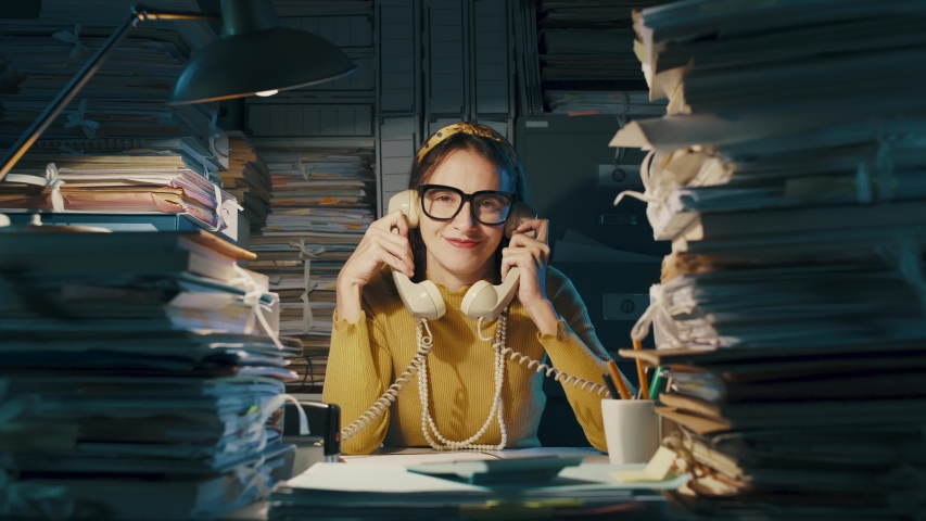 Smiling funny secretary answering phone calls in the office, she is holding two telephone receivers and nodding Royalty-Free Stock Footage #1040314415