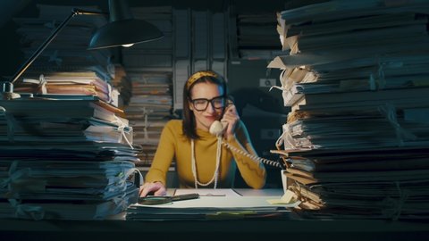 Angry stressed businesswoman sitting at office desk overloaded with paperwork, she screams at the phone