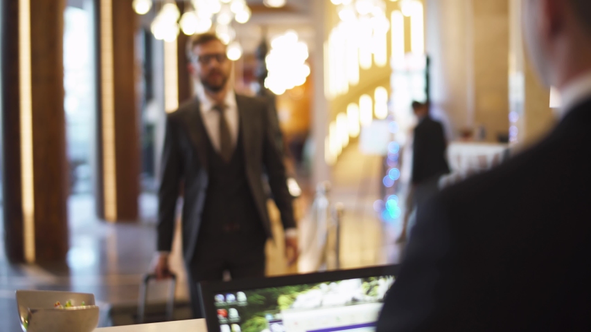 Businessman in suit carrying a suitcase man goes to reception of hotel and receives a key card from the room, business trip. Royalty-Free Stock Footage #1040322002