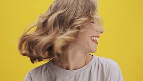 Attractive young woman with red lips laughing and shaking her head with her hair over yellow background isolated