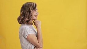 Positive young woman with red lips stands sideways and points a finger straight over yellow background isolated