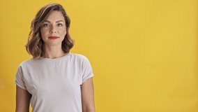 Beautiful young woman with red lips smiling and pointing with finger to the side and making thumb up gesture in another while looking at the camera over yellow background isolated
