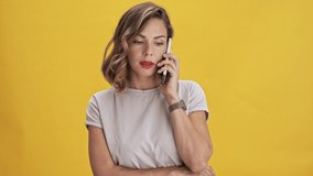 Beautiful young woman with red lips talking on mobile phone and smiling while standing over yellow background isolated