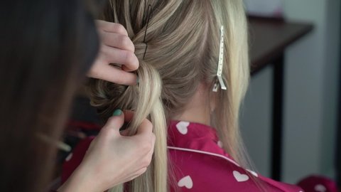 The hairdresser does the bride's hair. Wedding hairstyle for a young girl. Stylist doing hair styling.