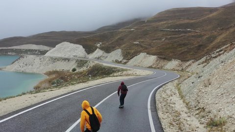 Two skateboarders rides on the road along mountains