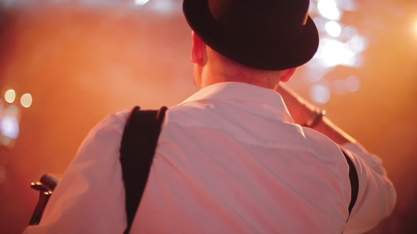 Back middle view of accordionist in hat and white shirt on stage