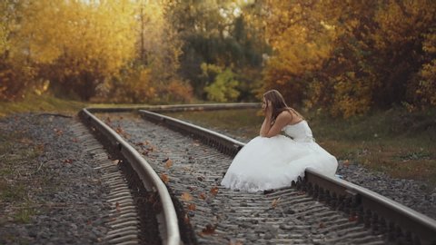 Runaway bride. sad girl sitting on rails in wedding dress