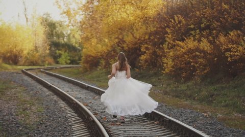 Runaway bride. Young girl running on railway in wedding dress. 