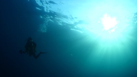 scuba diver silhouette underwater with sun beams and sun rays strong sun shine slow motion