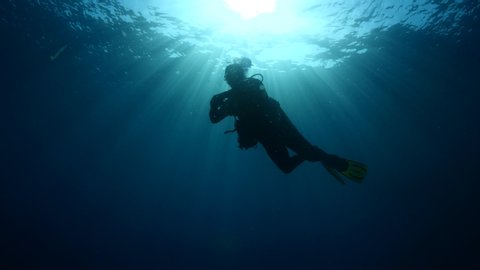 scuba diver silhouette underwater with sun beams and sun rays strong sun shine ocean scenery