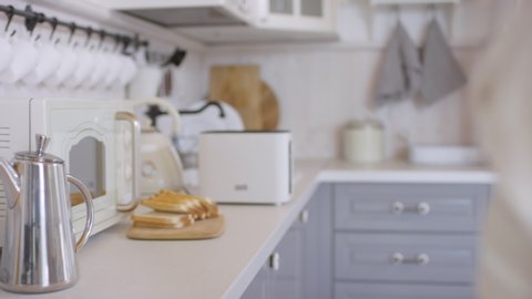 Dolly-in shot with mid-section of unrecognizable woman putting slices of bread into toaster : vidéo de stock