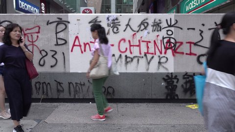 HONG KONG – 7 OCTOBER 2019: Pedestrians walk past damaged MTR station in Kowloon, with provocative political statement comparing China with Nazi Germany, after heavy protests in Hong Kong