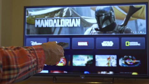Barcelona, Spain. November 2019: Man holds a remote control With the new Disney+ screen on TV, showing The Mandalorian space western television series. .Illustrative editorial. Disney+ is an online