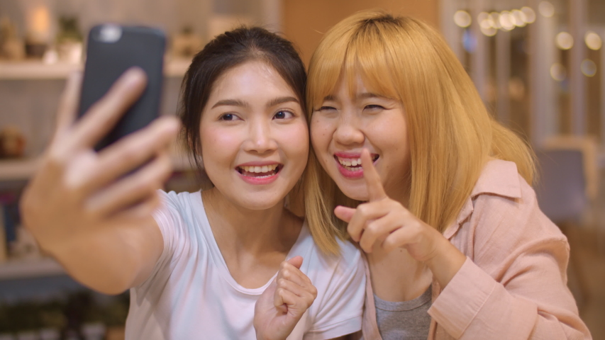 Lesbian lgbtq women influencer couple waving hand making video call at night cafe. Asian lover lady happy relax fun using technology phone record vlog video upload in social media at college campus. Royalty-Free Stock Footage #1040351327