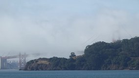 The Golden Gate Bridge shrouded by moving clouds on a foggy morning, seen from across Richardson Bay