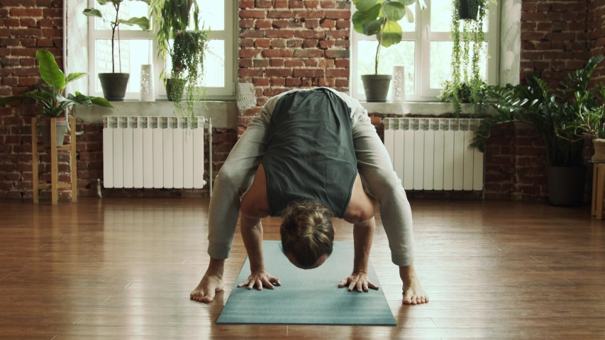 Man practice yoga pose in studio with brick wall and green plants. Fitness and healthy lifestyle concept. Bearded male making balance yoga pose in gym in slow motion. Find his harmony inside.  Royalty-Free Stock Footage #1040355896