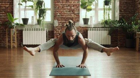 Man practice yoga pose in studio with brick wall and green plants. Fitness and healthy lifestyle concept. Bearded male making balance yoga pose in gym in slow motion. Find his harmony inside. 