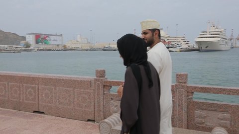 Muscat, Oman, - February 2019. A local couple - an oriental man and woman in Arabic clothes are walking along the city's promenade. Enjoy the views of the city.