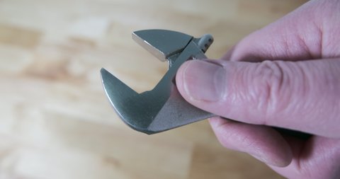 Adjustable spanner or wrench being closed, close up. Being held in the hand of a man. Wooden table in background.