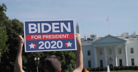 A man holds a Joe Biden 2020 election protest sign in front of the White House on a sunny summer day.  	